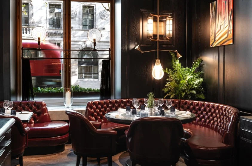 A dark and intimate restaurant dining area with a plush, red leather, button-tufted banquette and armchairs.