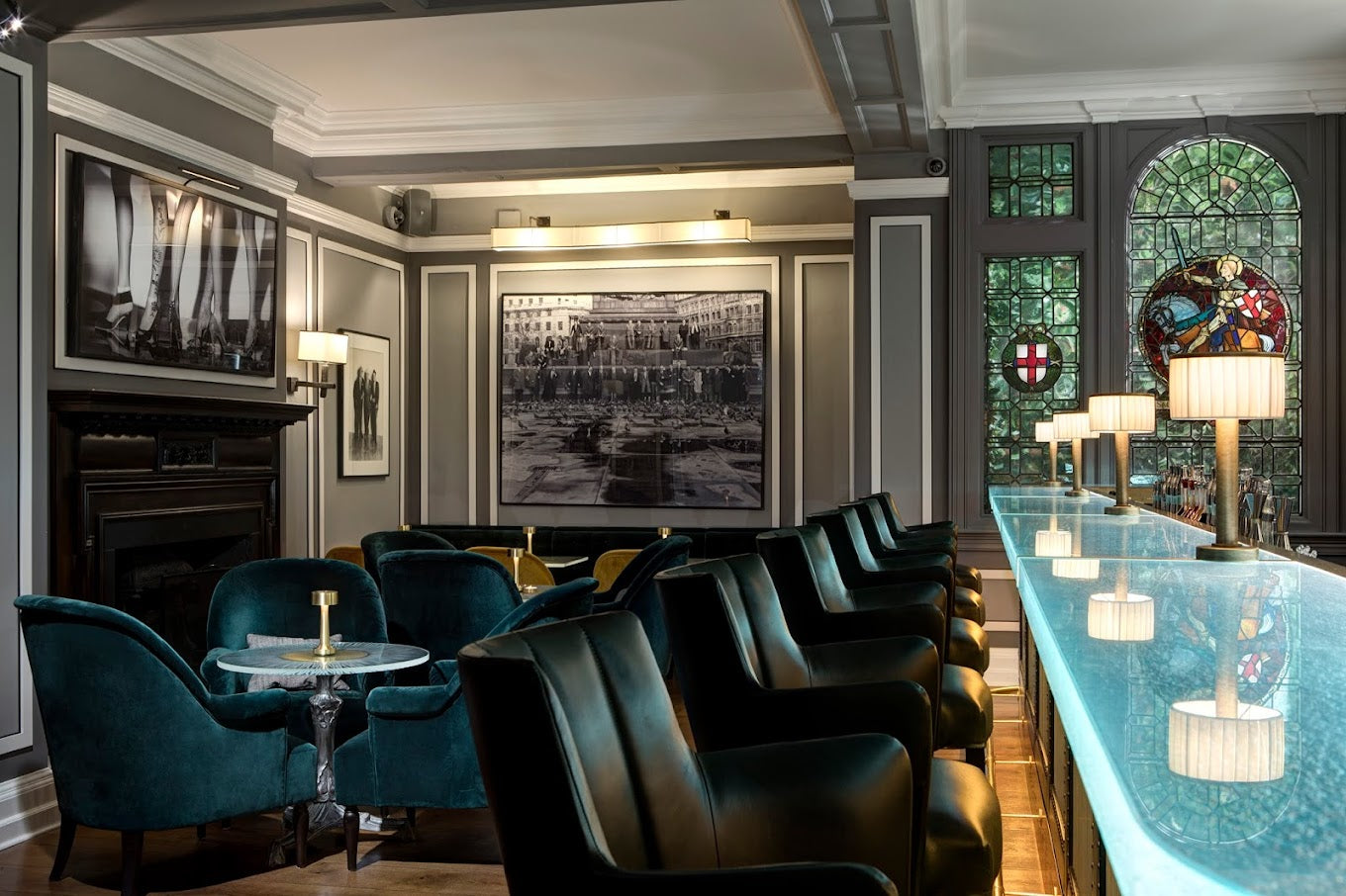 The Donovan bar cocktail bar in Mayfair, with teal velvet armchairs, a counter with a backlit blue top, and a stained-glass window.