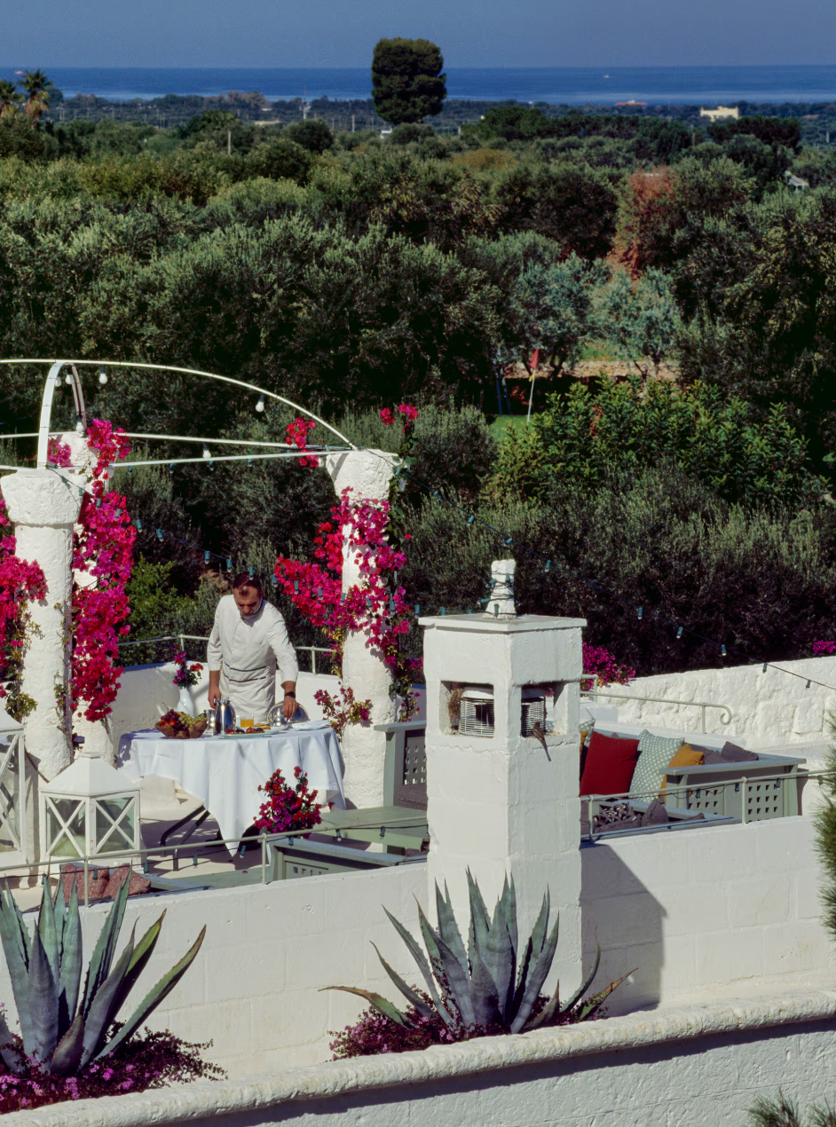 A rooftop terrace decorated with pink bougainvillea overlooking a lush, green landscape and the sea, at Masseria Torre Maizza in Puglia.