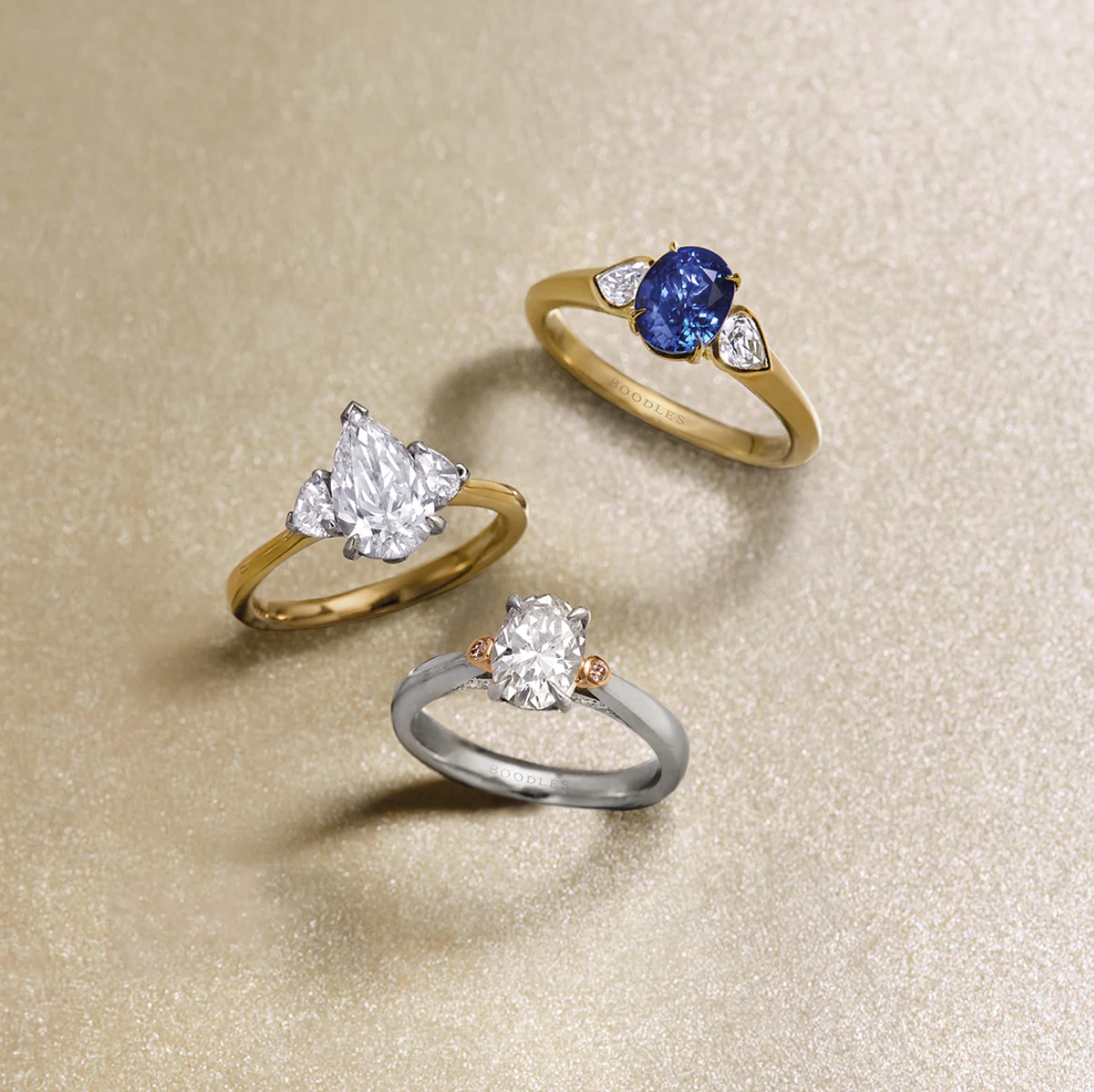 Three ornate rings with large jewels, set on a glittering gold background.