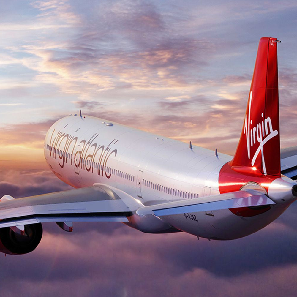 An image of a Virgin Atlantic airplane with its distinctive red tail fin flying into a beautiful sunset.